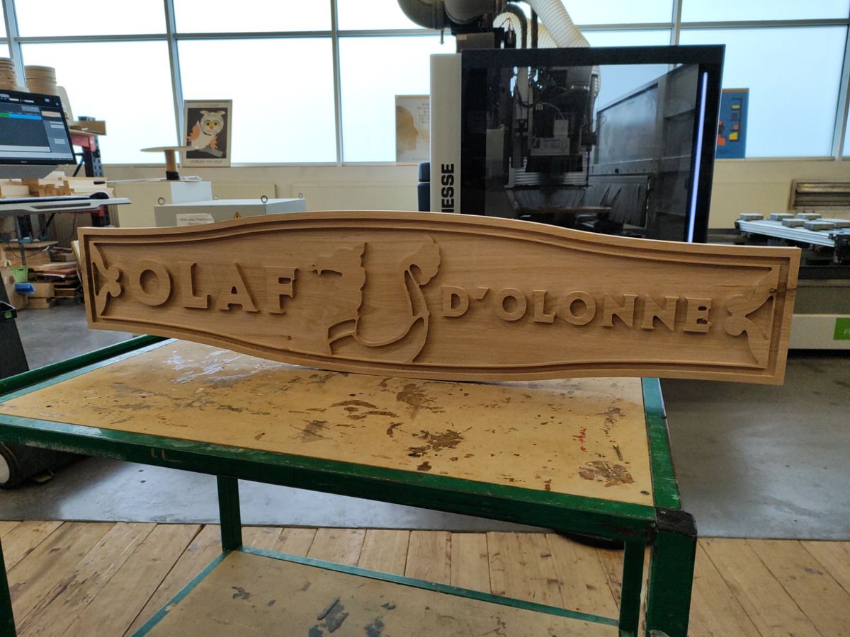 Plaque en bois gravée au nom d’Olaf d’Olonne, posée sur un établi d’atelier